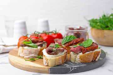 Bruschettas with roast beef, cream cheese, basil, sun-dried tomatoes and fresh vegetables on white marble table, closeup