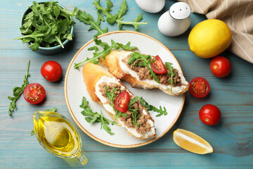 Delicious bruschettas with tuna, tomatoes, arugula, lemons and oil on light blue wooden table, flat...