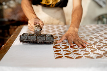 close up of batik maker pressing copper stamp ( BATIK CAP ) dipped in hot wax onto fabric, capturing manual craftsmanship and traditional textile printing in Pekalongan, Indonesia.