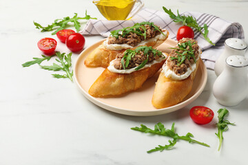 Delicious bruschettas with tuna, tomatoes and arugula on white marble table