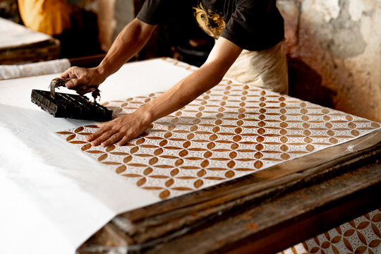 Close-up of artisan making batik using copper stamp (batik cap) on white fabric in Pekalongan, Indonesia, showing traditional craftsmanship and cultural textile process.