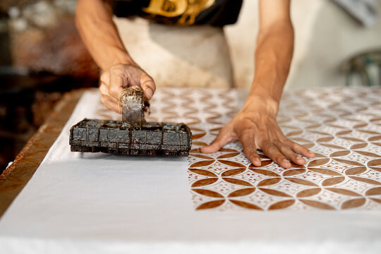 close up of batik maker pressing copper stamp ( BATIK CAP ) dipped in hot wax onto fabric, capturing manual craftsmanship and traditional textile printing in Pekalongan, Indonesia.