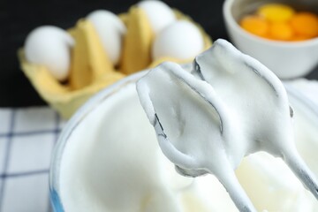 Whipped egg whites in bowl, ingredients and hand mixer on table, closeup