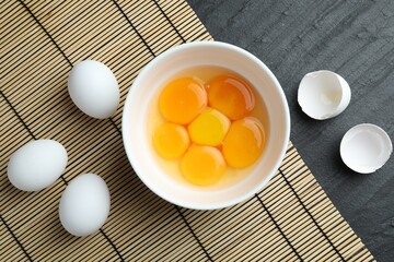 Raw eggs and yolks on black table, flat lay