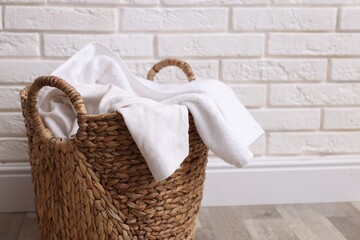 Wicker basket full of laundry on floor near white brick wall indoors, closeup. Space for text