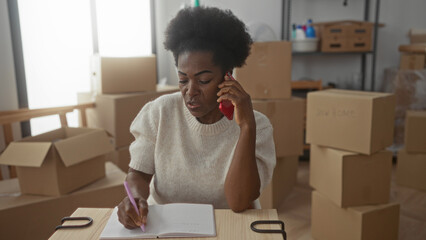 Woman talking on phone and writing in notebook surrounded by boxes in new home living room.