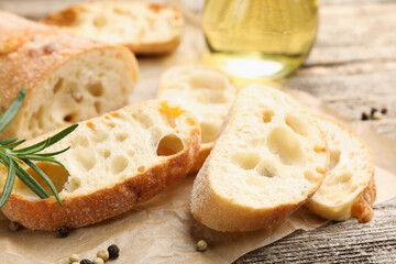 Ciabatta slices, oil, peppercorns and rosemary on wooden table, closeup