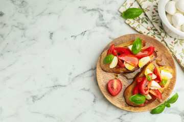 Tasty bruschettas with mozzarella cheese, tomatoes and basil on white marble table, flat lay. Space for text
