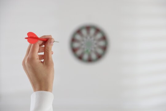 Woman with dart aiming at dartboard indoors, selective focus