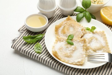 Delicious ravioli with cream sauce and basil served on white table, closeup