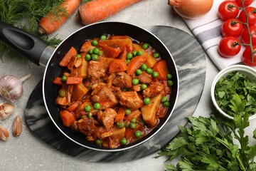 Delicious cooked stew in frying pan and ingredients on grey table, flat lay
