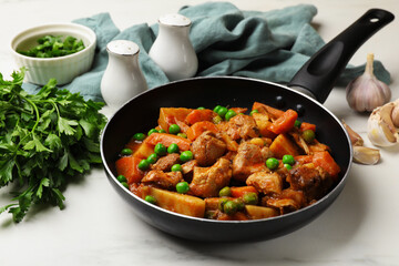 Delicious cooked stew in frying pan, parsley and garlic on white marble table, closeup