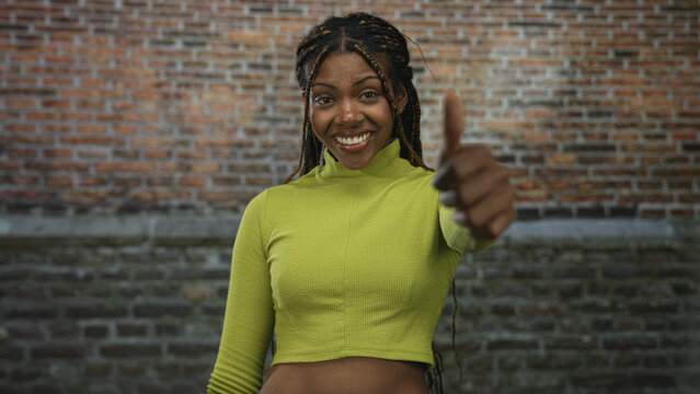 African american woman in green cropped top smiling then frowning while giving thumbs up then thumbs down in building; confidence decision.