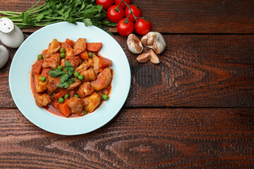 Delicious cooked stew and ingredients on wooden table, flat lay. Space for text