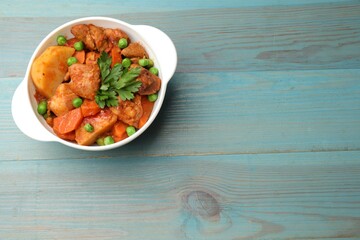 Delicious cooked stew in bowl on light blue wooden table, top view. Space for text