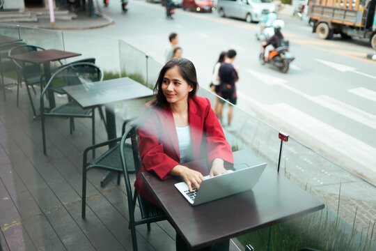 Asian woman working on laptop in urban street cafe - Powered by Adobe