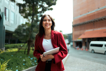 Asian businesswoman walking outdoors holding tablet smiling confidently
