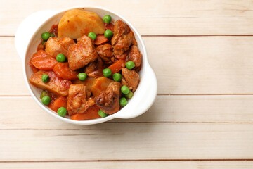 Delicious cooked stew in bowl on light wooden table, top view. Space for text
