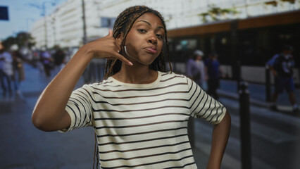 Fototapeta premium Woman points finger at camera on a busy street wearing a striped shirt and braids; confidence urban attitude.
