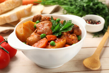 Delicious cooked stew served on light wooden table, closeup