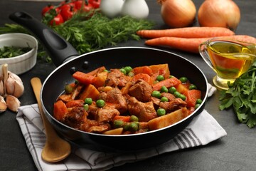 Delicious cooked stew in frying pan and ingredients on black table, closeup
