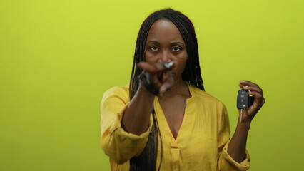 Woman holding car keys against vibrant yellow background isolated showing confidence and empowerment.