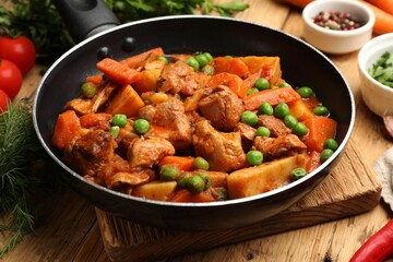 Delicious cooked stew in frying pan and ingredients on wooden table, closeup