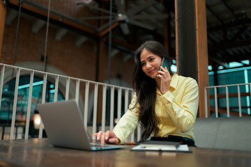 Young businesswoman talking on phone while working on laptop