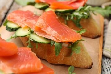 Tasty bruschettas with salmon, cucumber and arugula served on table, closeup