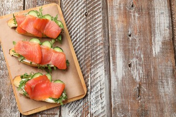 Tasty bruschettas with salmon, cucumber and arugula served on wooden table, top view. Space for text