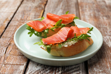 Tasty bruschettas with salmon and arugula served on wooden table, closeup