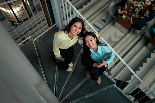 Two smiling businesswomen standing on modern spiral stairs - Powered by Adobe