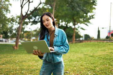 Fototapeta premium Young Asian woman using laptop outdoors in park