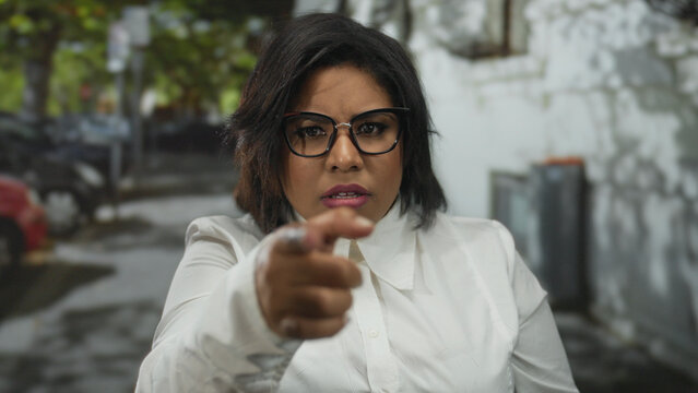 Woman outdoors on city street displaying surprise while gesturing incredulously, wearing glasses and white shirt, capturing expressions of disbelief and emotion. - Powered by Adobe