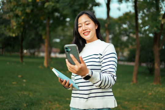Asian student smiling viewing smartphone in park