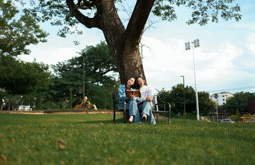 Students reading book together sitting under tree