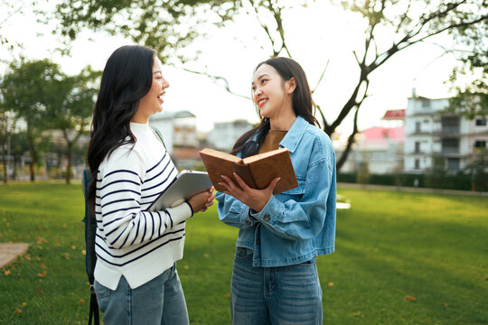 Young female students discussing while holding book and tablet