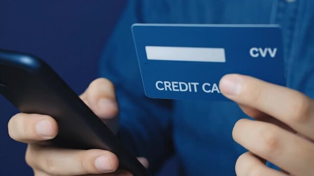 Close-up of hands holding a credit card and smartphone, focusing on secure online shopping, mobile payment, and e-commerce transactions with CVV en...