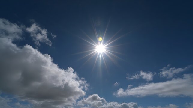 The brilliant sun shines brightly in a clear blue sky casting radiant rays and illuminating scattered white clouds