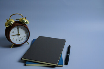 Still life of vintage alarm clock, note book and pen neatly arranged on grey background for desk office concept, productivity concept and time management concept