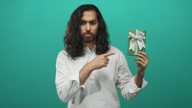 Man pointing index finger while holding green gift box against teal studio background; caution promotion.