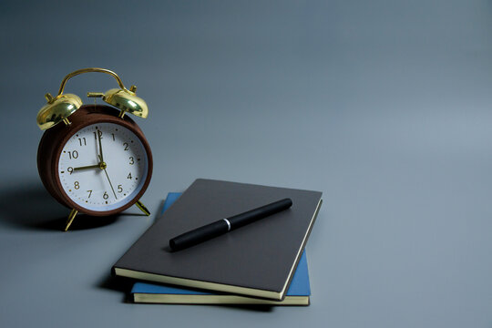 Classic alarm clock with notebooks and pen on grey surface, symbol of planning, focus and daily productivity