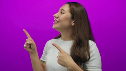 Obraz premium Hispanic young woman smiling and pointing both index fingers to the left in studio scene; excitement.