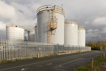Industrial Storage Tanks Complex With Large White Silos, Fenced Yard, and Brick Utility Buildings