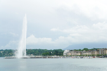 A large fountain is in the middle of a city Geneva Switzerland with a cloudy sky above