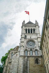 A large stone building in Geneva Switzerland with a clock tower and a red flag on top