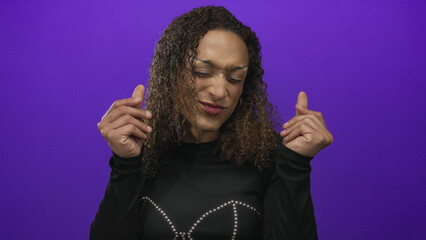Transgender hispanic woman makes money gesture with fingers in a purple studio set; greed wealth desire.