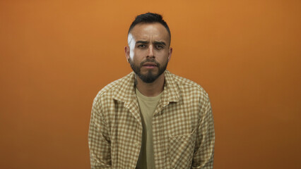 Obraz premium Man frowning with visible face and beard, leaning slightly forward in an orange studio; introspection.