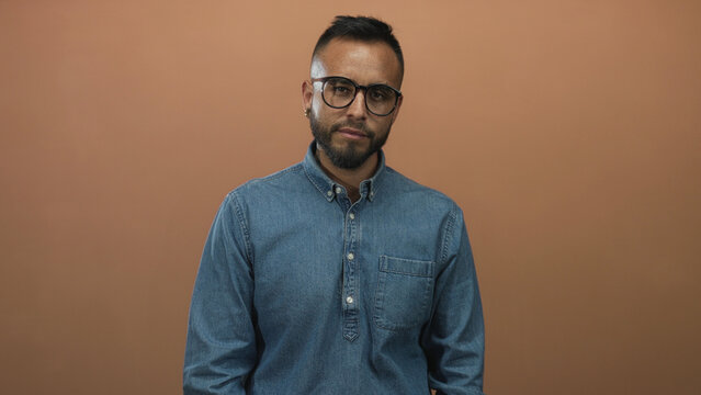 Man with glasses tilting his head in a studio against a warm brown backdrop; thoughtful introspection.