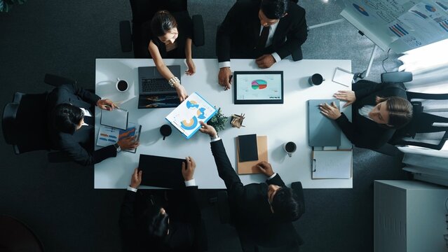Top view of smart diverse team walk at meeting table and start to discuss about financial statistic. Group of business people prepare for meeting while looking at stock market document. Directorate.